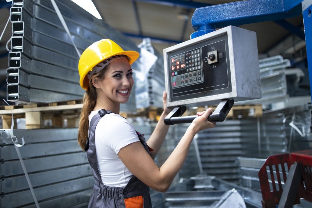 portrait of female factory worker operating industrial machine and setting parameters on the computer.