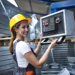 portrait of female factory worker operating industrial machine and setting parameters on the computer.